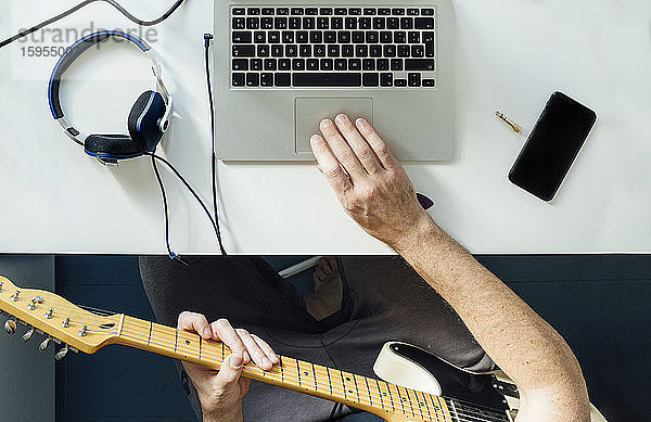 Draufsicht eines Mannes,  der online mit einem Laptop Gitarre lernt