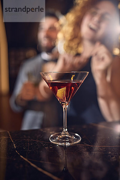 Cocktailglas auf der Theke in einer Bar mit glücklichen Menschen im Hintergrund