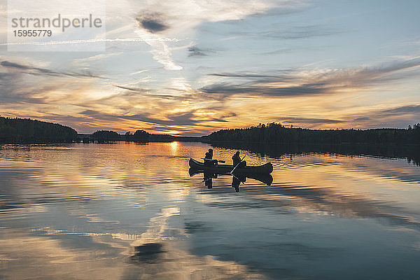 Junge Leute fahren bei Sonnenuntergang auf dem See Boot