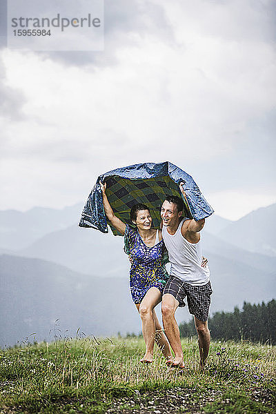 Glückliches Paar läuft bei Regen auf einer Bergwiese,  Achenkirch,  Österreich