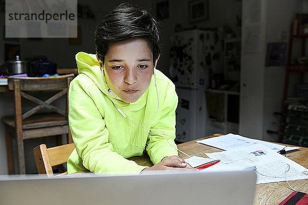 Ein Junge sitzt an einem Schreibtisch und benutzt einen Laptop für eine interaktive Lernsitzung,  Hausunterricht,  harte Arbeit.