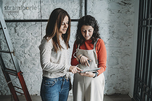 Zwei mittelgroße erwachsene Frauen schauen sich in ihrem neuen Geschäft ein digitales Tablet an