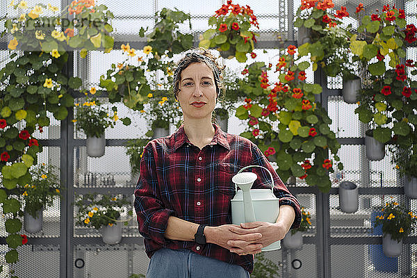 Porträt einer Frau mit Gießkanne vor Blumen in einer Gärtnerei