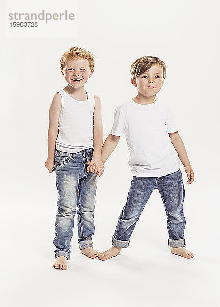 Porträt von zwei kleinen Jungen,  die sich vor einem weißen Hintergrund an den Händen halten