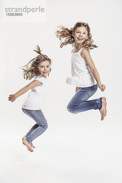 Porträt von zwei barfuß Schwestern springen in der Luft vor weißem Hintergrund