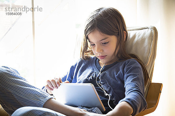 Mädchen sieht sich ein Online-Video an,  während sie zu Hause auf einem Sessel am Fenster sitzt
