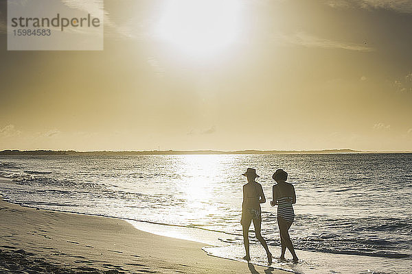 Rückansicht von Freundinnen beim Spaziergang am Strand von Grace Bay bei Sonnenuntergang,  Providenciales,  Turks- und Caicosinseln