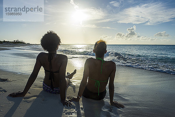 Rückansicht von Freundinnen,  die bei Sonnenuntergang am Strand von Grace Bay auf das Meer blicken,  Providenciales,  Turks- und Caicosinseln