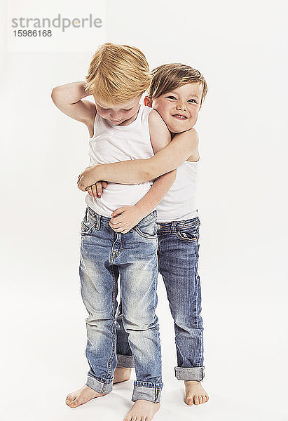 Porträt eines kleinen Jungen,  der einen anderen kleinen Jungen umarmt,  vor einem weißen Hintergrund