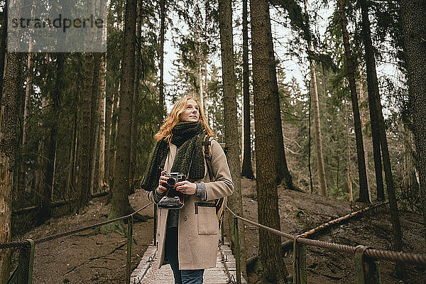 Gelassene rothaarige Frau mit Kamera auf Waldsteg