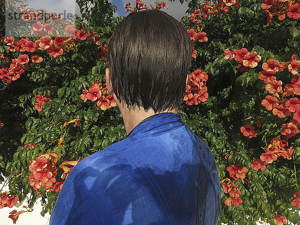 Frau mit nassem Haar steht an Blumen im sonnigen Garten
