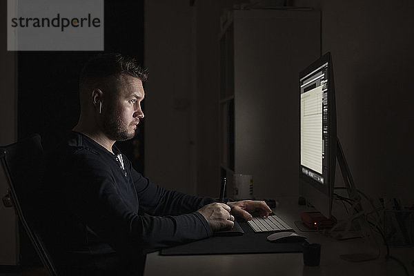 Mann mit Ohrstöpseln arbeitet spät am Computer in einem dunklen Raum