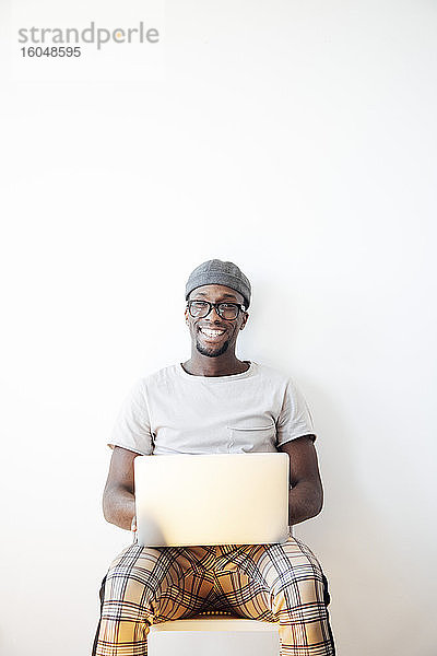 Glücklicher junger Mann sitzt mit Laptop vor weißem Hintergrund