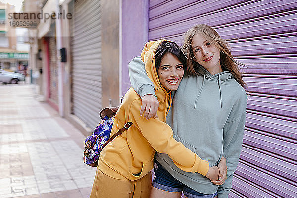 Porträt von zwei lächelnden und sich umarmenden Freundinnen in der Stadt