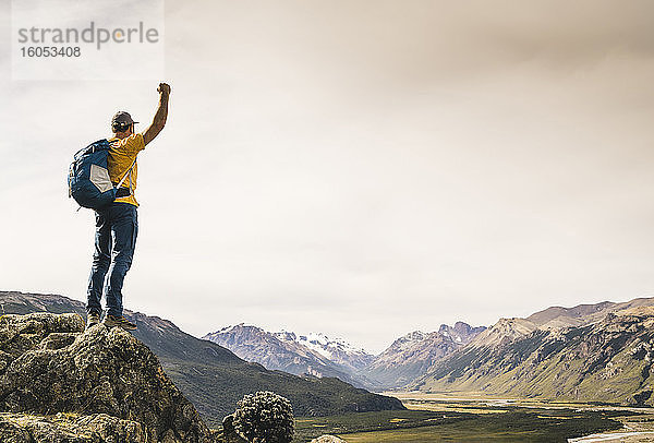 Mann mit erhobenem Arm,  der auf einem Felsen stehend die Berge betrachtet,  Patagonien,  Argentinien