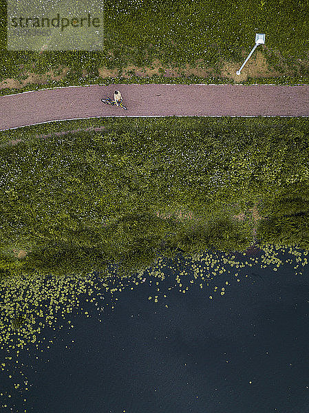 Russland,  Tichwin,  Luftaufnahme einer Radfahrerin,  die auf einem Fußweg am Seeufer im Park eine Pause einlegt