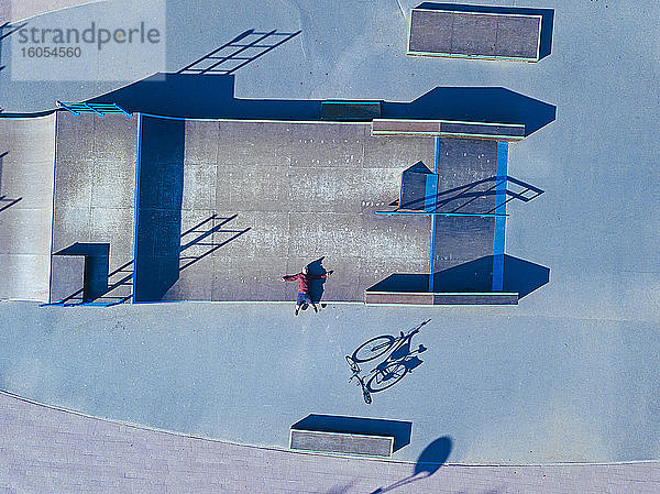 Mann liegt auf Betonrampe in Skatepark,  Luftaufnahme