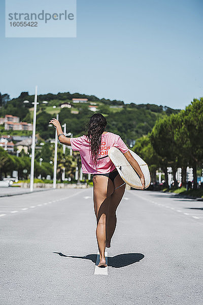 Rückansicht einer Surferin mit Surfbrett auf der Straße