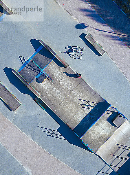 Mann sitzt auf Betonrampe in Skatepark,  Luftaufnahme