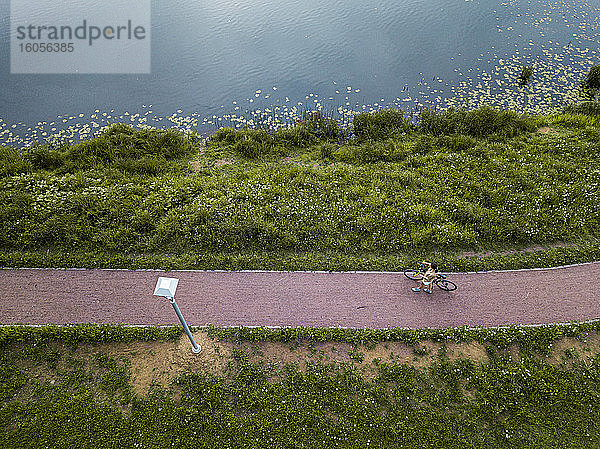 Russland,  Tichwin,  Luftaufnahme einer Radfahrerin,  die auf einem Fußweg am Seeufer im Park eine Pause einlegt