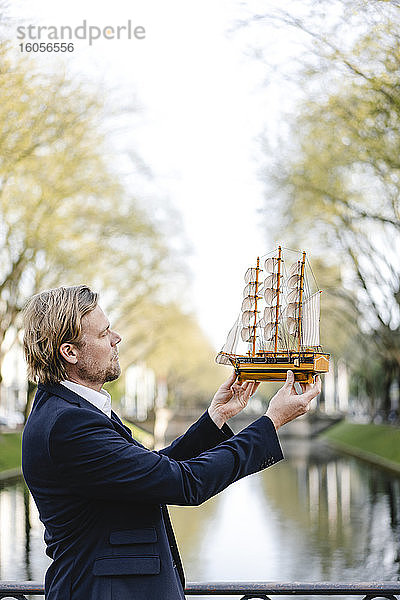 Geschäftsmann hält Modellschiff an einem Kanal