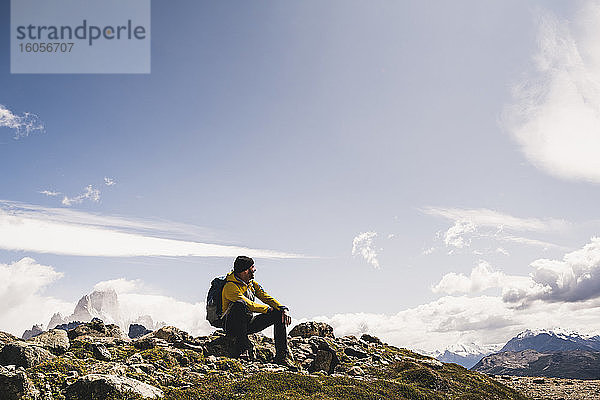 Männlicher Wanderer auf einem Berg sitzend gegen den Himmel an einem sonnigen Tag,  Patagonien,  Argentinien