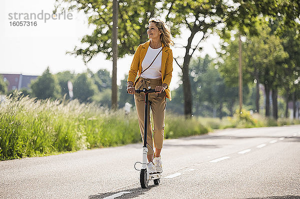 Ältere Frau fährt elektrischen Roller auf der Straße an einem sonnigen Tag