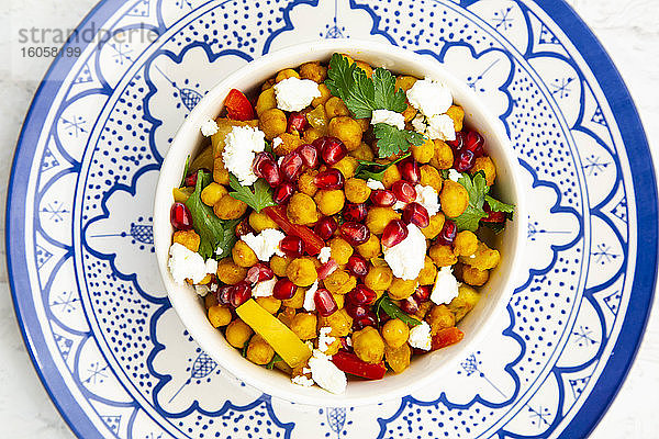 Schüssel mit vegetarischem Salat mit Kichererbsen,  Kurkuma,  Paprika,  Tomaten,  Petersilie,  Feta-Käse und Granatapfelkernen