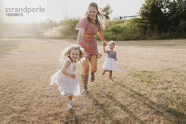 Glückliche Mutter läuft mit Töchtern auf einer Wiese im Gegenlicht
