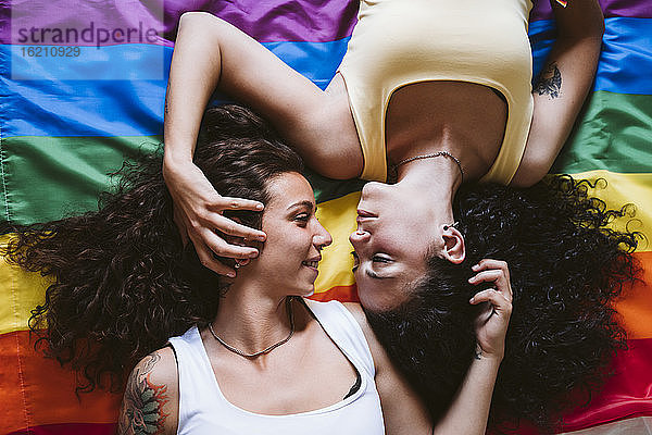 Romantisches lesbisches Paar,  das sich gegenseitig anschaut,  während es auf der Regenbogenflagge liegt