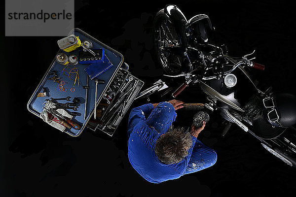 Draufsicht auf einen Mann,  der ein altes Motorrad repariert,  mit schwarzem Hintergrund (Ardie RZ)