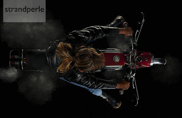 Draufsicht einer Frau auf einem alten Motorrad mit schwarzem Hintergrund und Rauch (Zuendapp KS 125 Sport)