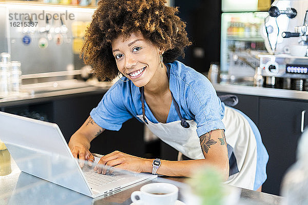 Glückliche Besitzerin mit Laptop am Tresen eines Cafés