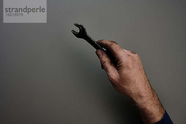 Draufsicht auf eine Hand,  die einen Schraubenschlüssel vor einem grauen Hintergrund hält