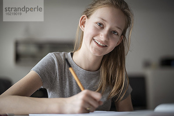Lächelndes Mädchen,  das zu Hause lernt und in ein Schulheft schreibt