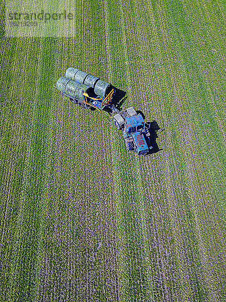 Luftaufnahme eines Traktors,  der Heuballen auf einem Feld einsammelt