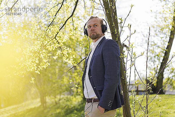 Männlicher Unternehmer hört Musik,  während er an einem sonnigen Tag in den Park blickt