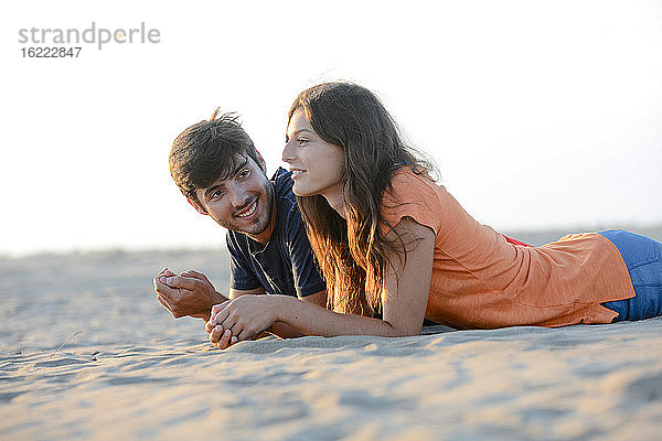 romantisches junges Paar in der Liebe zusammen liegend im Sand entlang des Strandes des Mittelmeers Sonnenuntergang