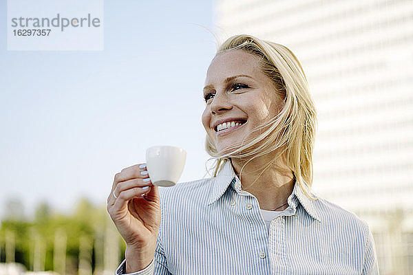 Lächelnde blonde Frau,  die eine Kaffeetasse hält und in den Himmel schaut