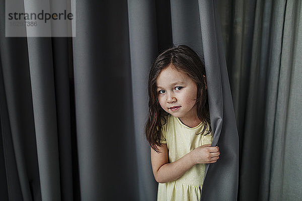 Nettes Mädchen steht gegen grauen Vorhang zu Hause