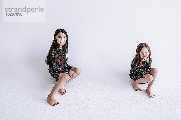 Lächelnde Schwestern sitzen vor weißem Hintergrund im Studio