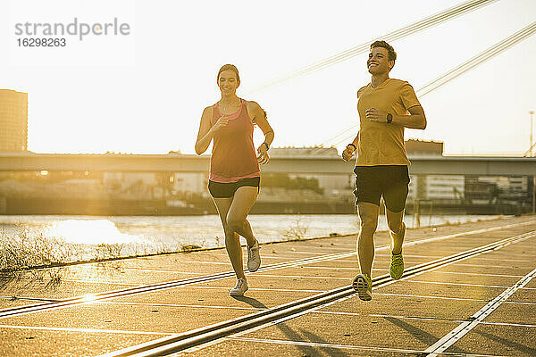 Lächelnder Mann und lächelnde Frau joggen am Hafen an einem sonnigen Tag