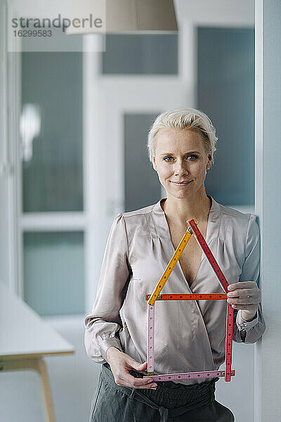 Selbstbewusste Architektin,  die ein Modell hält,  während sie im Büro steht
