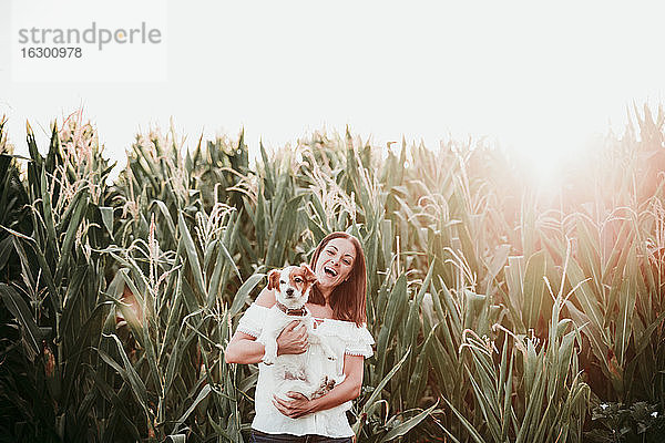 Glückliche Frau mit Hund im Kornfeld bei Sonnenuntergang