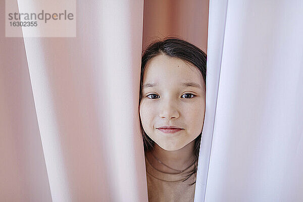 Mädchen versteckt sich zu Hause hinter einem Vorhang
