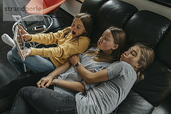 Drei Freundinnen sitzen auf einer Couch und machen ein Selfie mit einem digitalen Tablet.