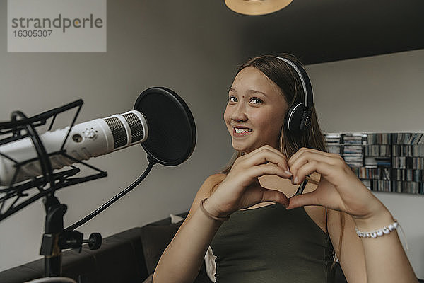 Lächelndes Teenager-Mädchen,  das beim Singen im Aufnahmestudio ein Herz formt