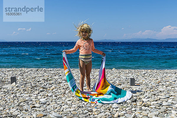 Porträt eines kleinen Mädchens am felsigen Strand mit Handtuch in den Händen