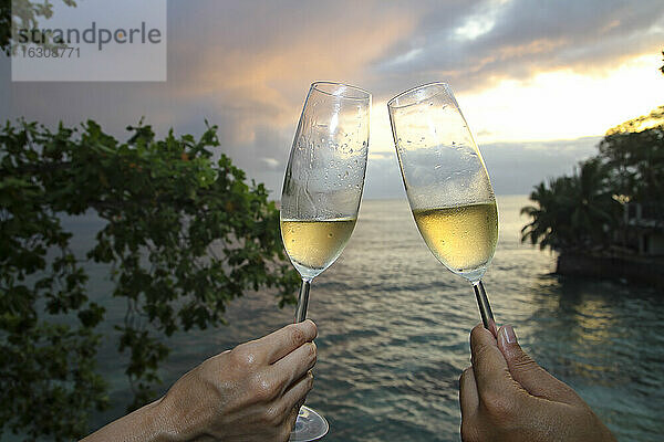 Zwei Menschen halten Champagnerflöten am Strand