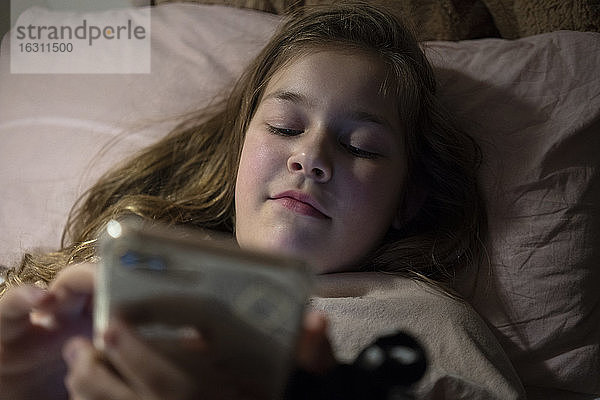 Mädchen,  das im Schlafzimmer liegend ein Smartphone benutzt
